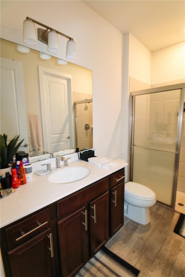 bathroom with toilet, a stall shower, vanity, and wood finished floors