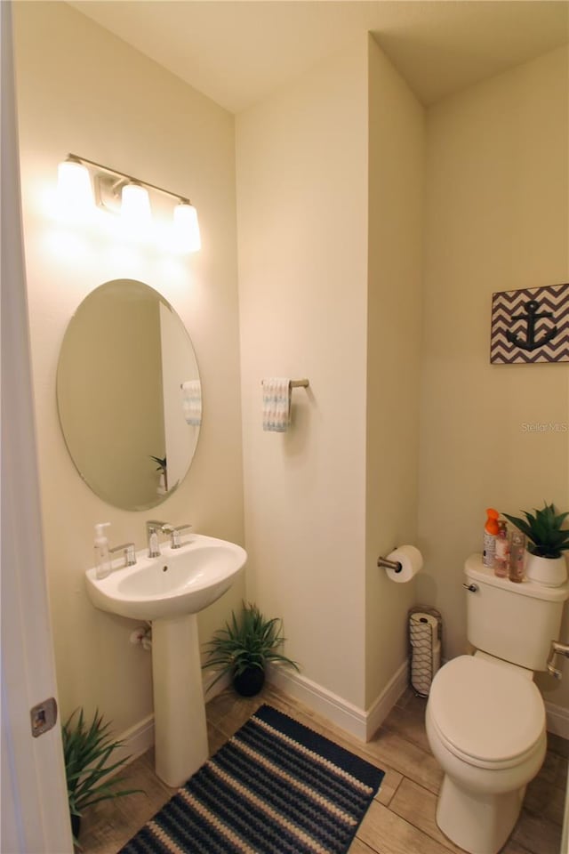 half bath with a sink, toilet, baseboards, and wood finish floors