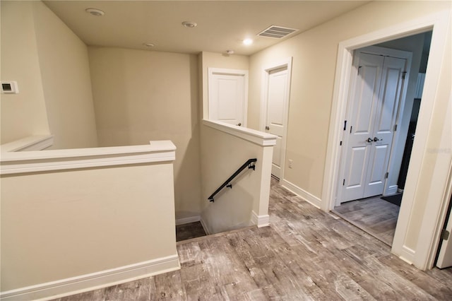 hall with an upstairs landing, visible vents, baseboards, and wood finished floors