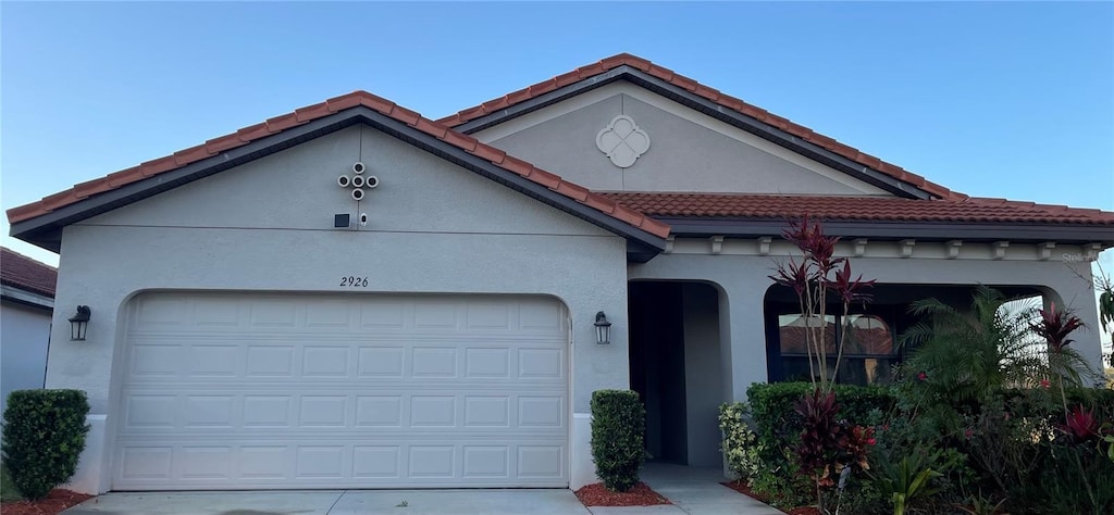 mediterranean / spanish home featuring a tile roof, an attached garage, concrete driveway, and stucco siding