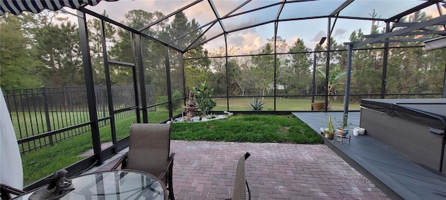 patio terrace at dusk with glass enclosure, fence, a yard, and a hot tub