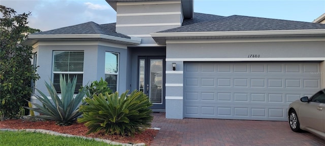 view of front of home with a garage, stucco siding, decorative driveway, and roof with shingles