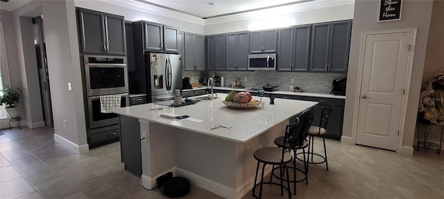 kitchen with a sink, stainless steel appliances, a kitchen bar, crown molding, and tasteful backsplash