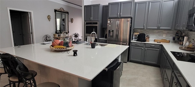 kitchen with a sink, light countertops, appliances with stainless steel finishes, a kitchen bar, and tasteful backsplash