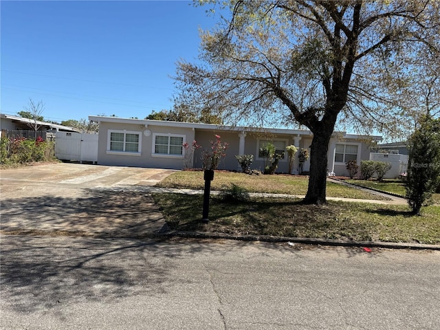 ranch-style house with stucco siding, a front lawn, driveway, and fence