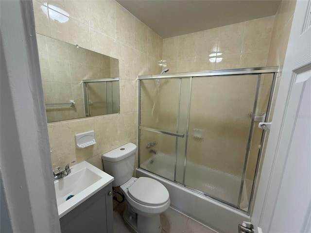 bathroom with toilet, tile walls, vanity, and shower / bath combination with glass door