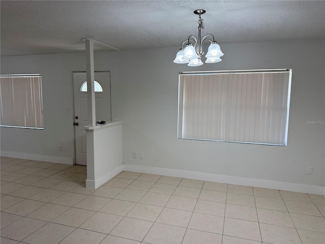 empty room featuring an inviting chandelier, light tile patterned flooring, baseboards, and a textured ceiling