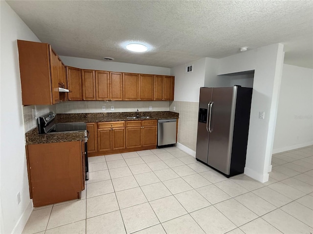 kitchen with under cabinet range hood, brown cabinets, appliances with stainless steel finishes, a textured ceiling, and a sink