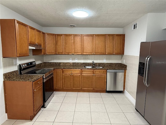 kitchen with a sink, under cabinet range hood, stainless steel appliances, brown cabinetry, and light tile patterned floors