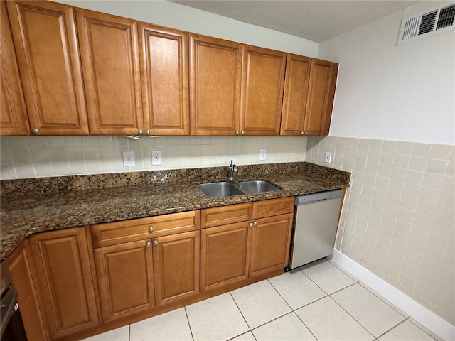 kitchen with brown cabinetry, visible vents, light tile patterned flooring, dishwasher, and tile walls