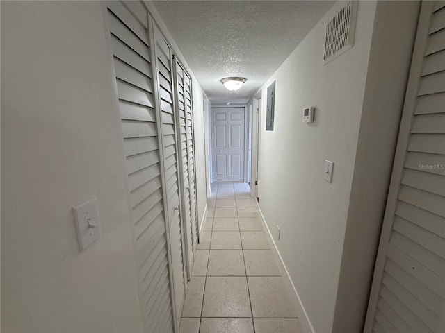 corridor with light tile patterned flooring, visible vents, a textured ceiling, and baseboards