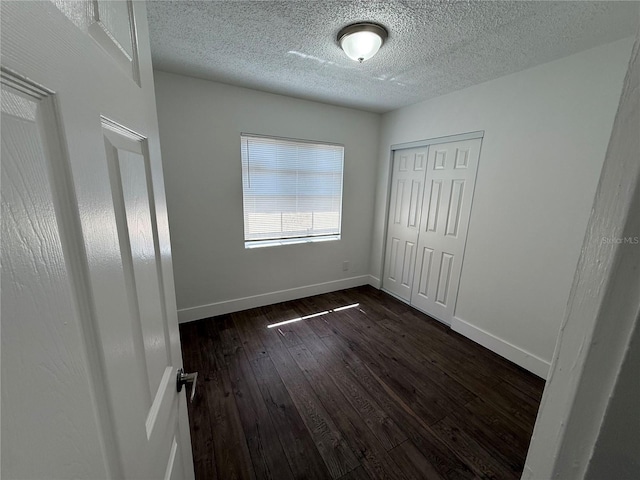 unfurnished bedroom with dark wood-style floors, a textured ceiling, a closet, and baseboards