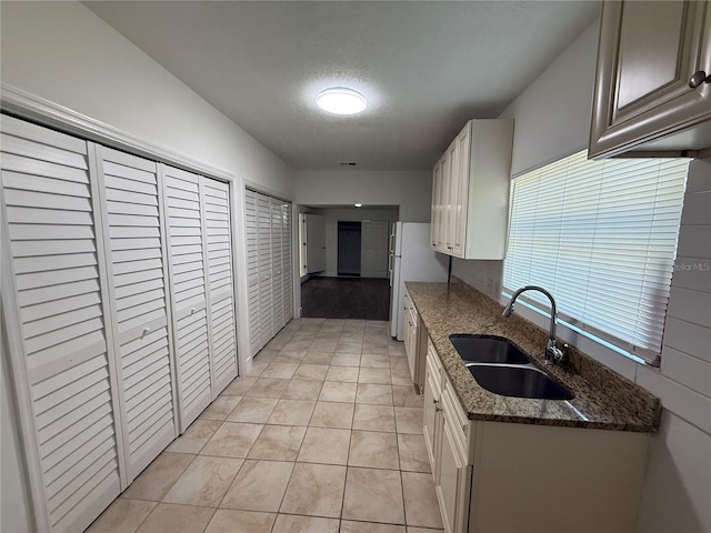 kitchen with visible vents, a sink, a textured ceiling, dark stone counters, and light tile patterned flooring