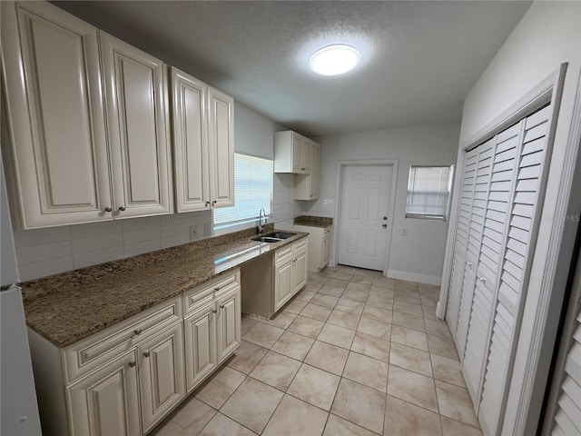 kitchen featuring a sink, a textured ceiling, stone counters, decorative backsplash, and light tile patterned floors