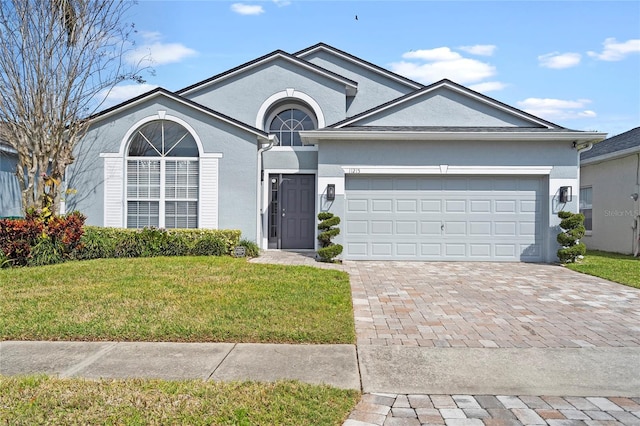 single story home featuring decorative driveway, a garage, a front lawn, and stucco siding