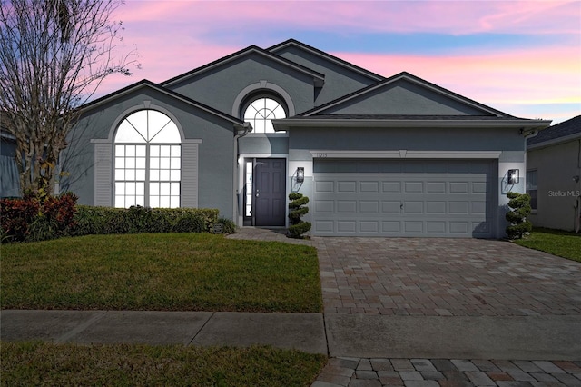 ranch-style home with decorative driveway, a yard, a garage, and stucco siding