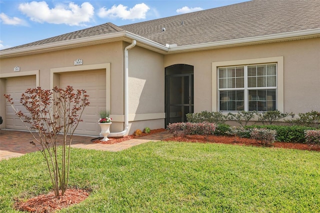 entrance to property featuring a garage, a lawn, roof with shingles, and stucco siding