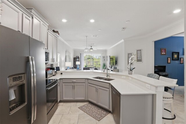 kitchen featuring a breakfast bar area, gray cabinets, a sink, stainless steel appliances, and crown molding