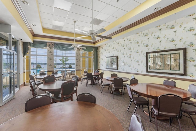 dining area featuring ornamental molding, a ceiling fan, carpet floors, wallpapered walls, and a raised ceiling