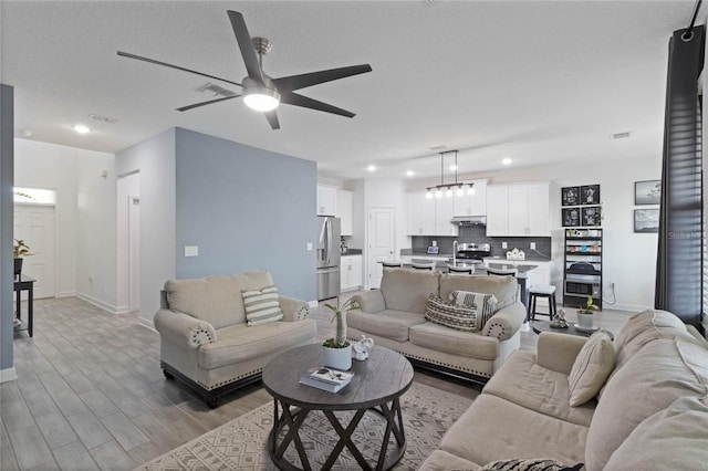 living room with visible vents, ceiling fan, light wood-type flooring, and baseboards