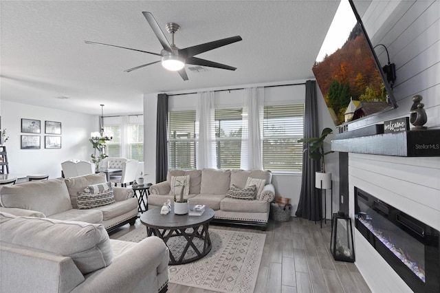 living area featuring light wood finished floors, ceiling fan with notable chandelier, a textured ceiling, and a large fireplace