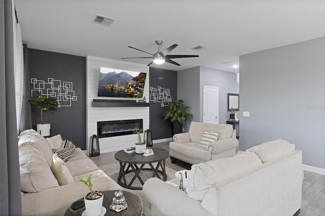 living area with baseboards, wood finished floors, visible vents, and a large fireplace