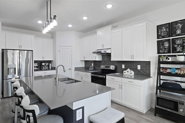 kitchen featuring a breakfast bar, a sink, under cabinet range hood, backsplash, and stainless steel appliances