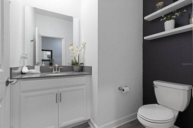 half bath featuring baseboards, toilet, wood finished floors, and vanity