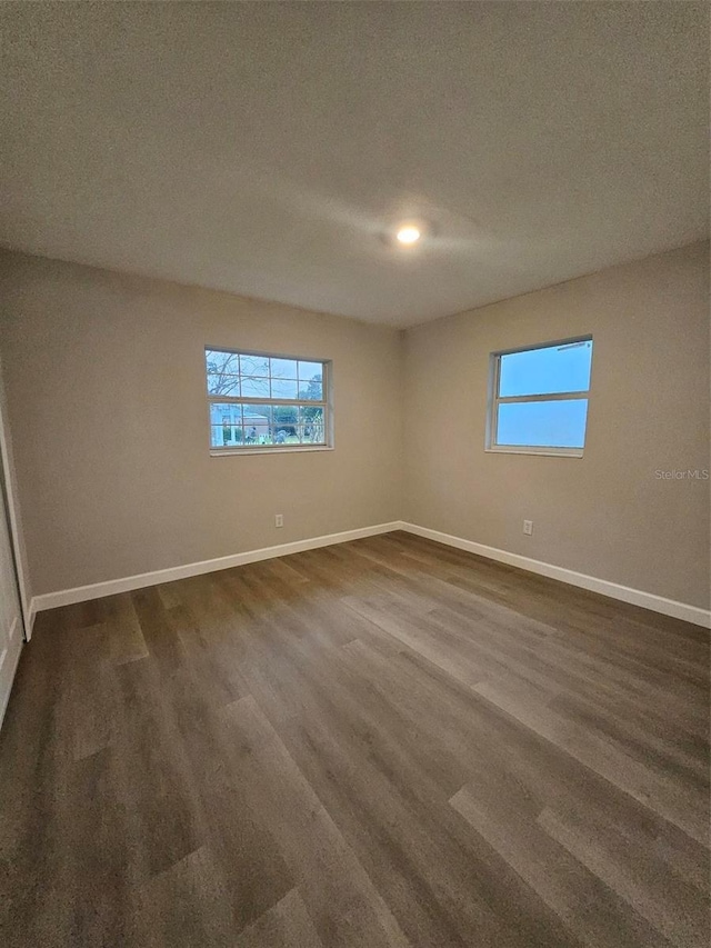 spare room with dark wood-style floors, a healthy amount of sunlight, and baseboards