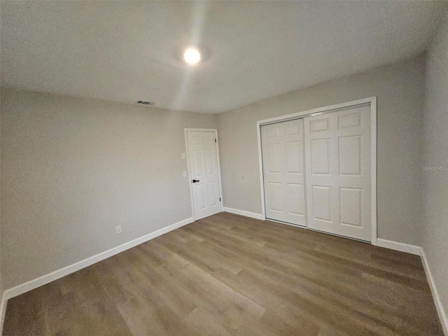 unfurnished bedroom featuring a closet, visible vents, baseboards, and wood finished floors