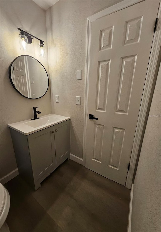 bathroom with vanity, wood finished floors, baseboards, toilet, and a textured wall