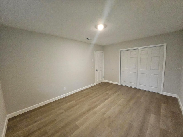 unfurnished bedroom with visible vents, baseboards, a closet, and wood finished floors