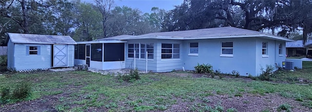 back of property with a storage unit, stucco siding, a lawn, an outdoor structure, and a sunroom