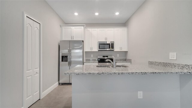 kitchen featuring light tile patterned floors, white cabinets, a peninsula, stainless steel appliances, and light stone counters
