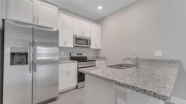 kitchen with light stone counters, a peninsula, white cabinetry, appliances with stainless steel finishes, and a sink