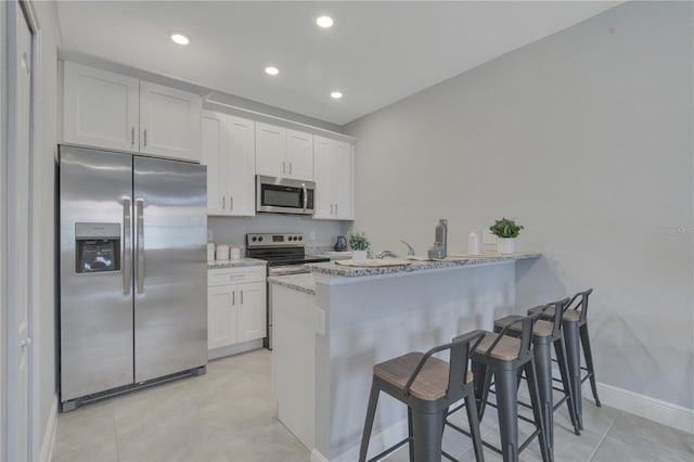kitchen featuring a peninsula, appliances with stainless steel finishes, white cabinetry, and a breakfast bar