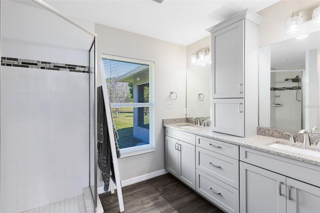 full bath with double vanity, a shower stall, wood finished floors, and a sink