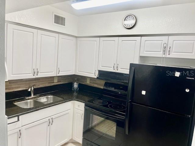 kitchen with visible vents, black appliances, a sink, dark countertops, and white cabinets