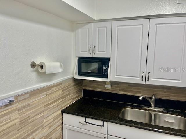 kitchen with a sink, dark countertops, white cabinets, and black microwave