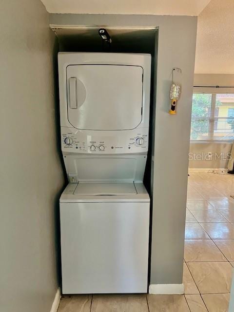 laundry area with light tile patterned floors, baseboards, laundry area, and stacked washer / dryer