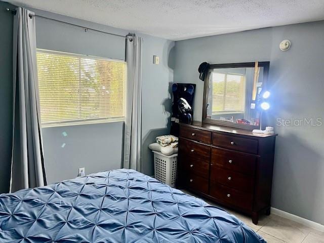 bedroom featuring light tile patterned floors, baseboards, and a textured ceiling