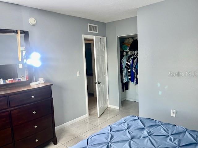 bedroom with light tile patterned floors, visible vents, baseboards, and a closet