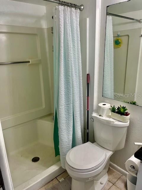 bathroom with tile patterned floors, toilet, and a shower stall