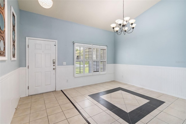 tiled entrance foyer featuring a notable chandelier and a wainscoted wall