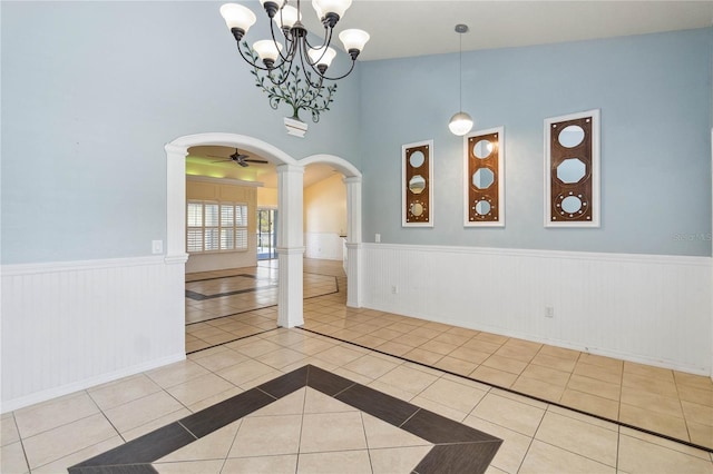 tiled spare room featuring decorative columns, arched walkways, a wainscoted wall, and a chandelier