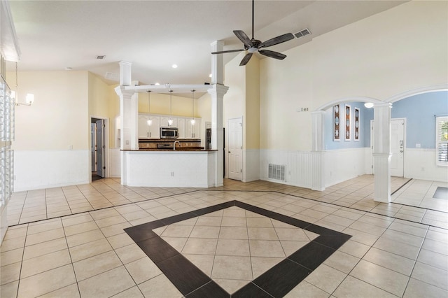 unfurnished living room with a ceiling fan, visible vents, decorative columns, light tile patterned flooring, and wainscoting