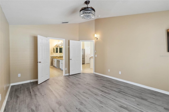 unfurnished bedroom featuring light wood finished floors, visible vents, baseboards, vaulted ceiling, and freestanding refrigerator