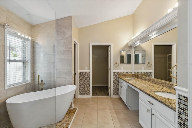 full bath with vaulted ceiling, double vanity, tile patterned floors, a soaking tub, and tile walls