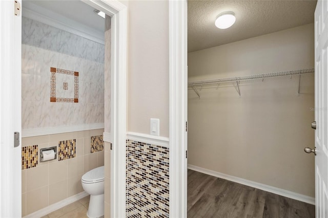 bathroom featuring wood finished floors, a spacious closet, a textured ceiling, tile walls, and toilet