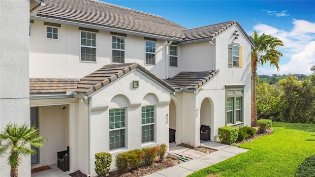 view of front of house with stucco siding, a front lawn, and a tile roof